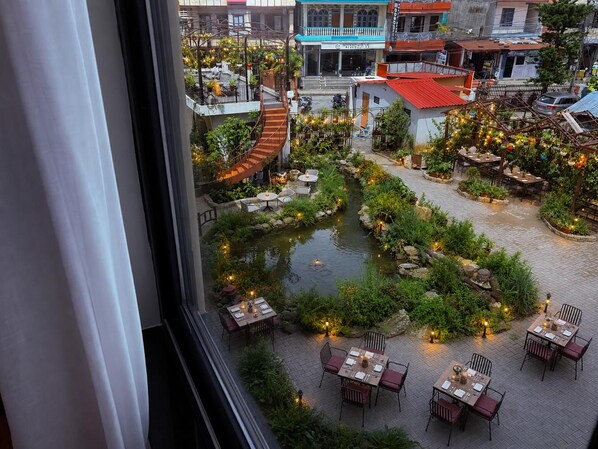 A courtyard with a central water feature, surrounded by tables and chairs, and buildings in the background.