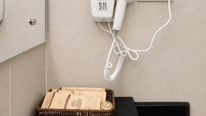 A hair dryer mounted on a wall with a power outlet, a black countertop, and a wicker basket with a paper bag on it. - Hotel Lumen - A Garden of Lights (Pokhara)