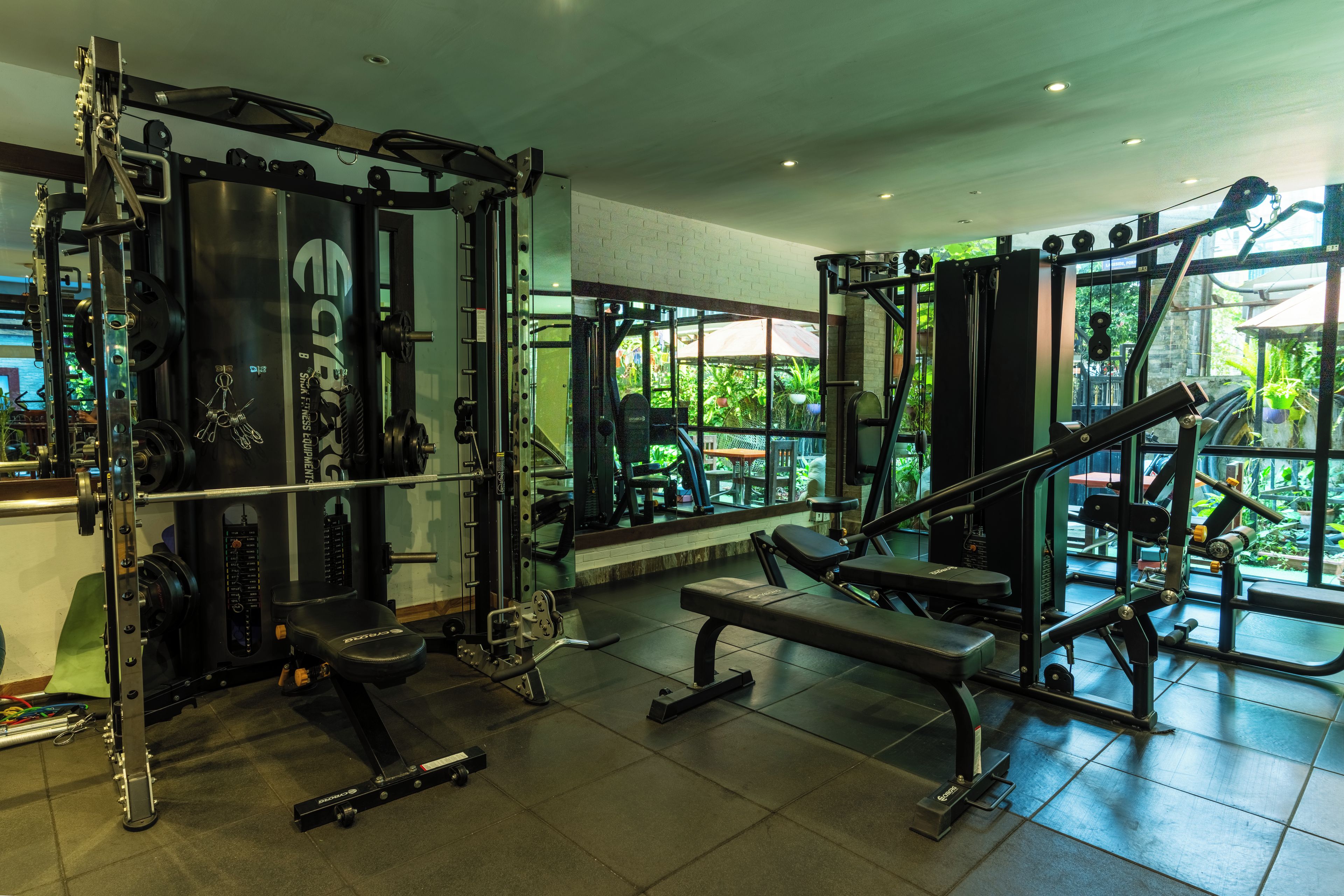 Un gimnasio con diversos equipos de ejercicio, incluyendo una jaula para sentadillas, bancos y accesorios para levantamiento de pesas.