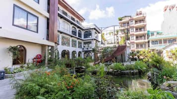 A courtyard with a water feature, surrounded by lush greenery and multi-story buildings with balconies.