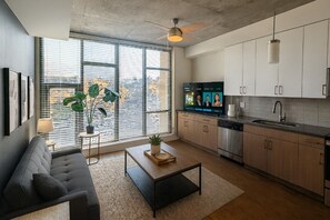 Een moderne keuken met een inbouwoven, een spoelbak en een televisie. Er is een groot raam met zonwering en een plant op de vensterbank.