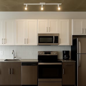 A modern kitchen with white cabinets, a stainless steel microwave, a black coffee maker, and a refrigerator. - Elegant 2BR High-Rise Stay | Downtown Birmingham S (Birmingham)