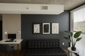 Une pièce moderne avec un mur gris foncé, un canapé en cuir noir, un bureau avec un ordinateur et des œuvres d’art abstraites encadrées.