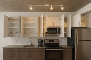A modern kitchen with open cabinets, a microwave, a refrigerator, a coffee maker, and a stove. - Elegant 2BR High-Rise Stay | Downtown Birmingham S (Birmingham)