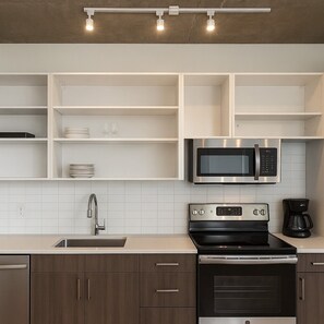 Een moderne keuken met witte kasten, een roestvrijstalen magnetron, een zwart fornuis en een koffiezetapparaat.