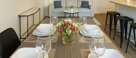 A dining room with a long table set for six, a ceiling fan, and a sofa in the background.