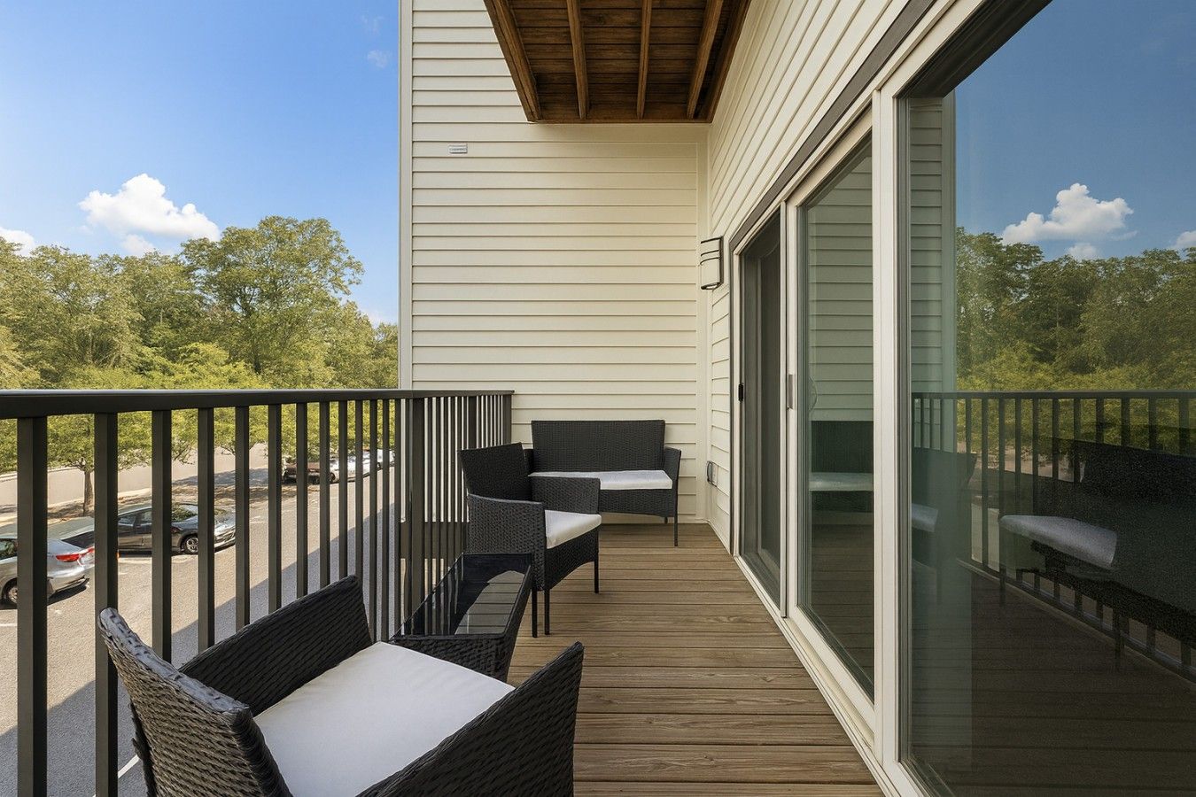 A balcony with wicker furniture, a wooden deck, and a view of trees and a parking lot.