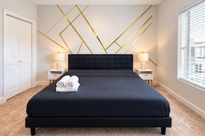 Ein Hotelzimmer mit einem großen Bett, zwei Nachttischen, einer Bettumrandung mit geometrischen Mustern und einem Fenster mit Jalousien.