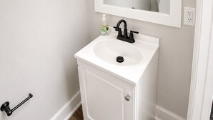A bathroom with a white sink, a mirror, and two light fixtures above the mirror. - Peaceful 2BR Townhome Near Birmingham (Hoover)