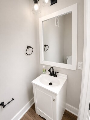 Une salle de bain avec un lavabo blanc, un miroir et deux luminaires placés au-dessus du miroir.