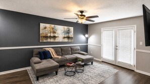 A living room with a sectional sofa, two side tables, a ceiling fan, and a painting on the wall. - Peaceful 2BR Townhome Near Birmingham (Hoover)