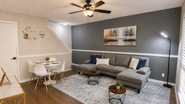 A living room with a grey sofa, two coffee tables, a dining table with chairs, a ceiling fan, and a painting on the wall. - Peaceful 2BR Townhome Near Birmingham (Hoover)