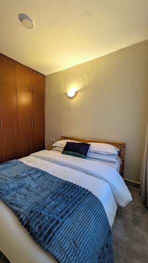 A bedroom with a bed, wooden wardrobe, and a wall-mounted light fixture.
