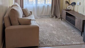 Ein Wohnzimmer mit einer Couch, einem Fernseher an der Wand und einem Fenster mit Vorhängen.