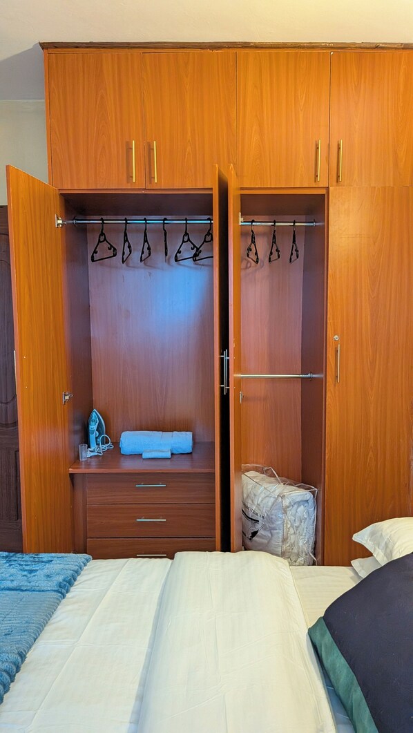 A bedroom with a wooden wardrobe, a bed, and a hanging clothes rack.