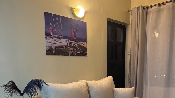 Ein Wohnzimmer mit einem beigen Sofa, einem Segelbootgemälde, einer Vase und einem kleinen Tisch mit einer Lampe.