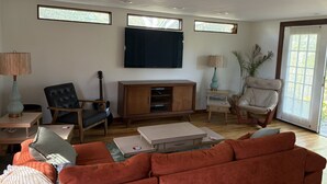 Ein Wohnzimmer mit einer Couch, einem Fernseher, einer Gitarre und einem Sessel.