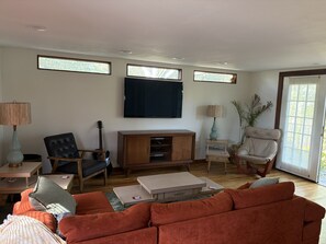 Ein Wohnzimmer mit einer Couch, einem Fernseher, einer Gitarre und einem Sessel.
