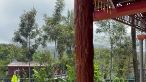 A wooden railing with a view of a lush garden and a building in the background. - Venkataramana KV (Mekeri)