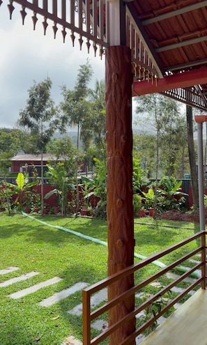A wooden railing with a view of a lush garden and a building in the background. - Venkataramana KV (Mekeri)