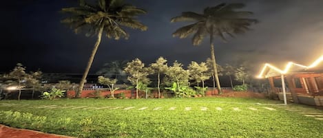 A nighttime outdoor area with a well-maintained lawn, palm trees, and a paved walkway.