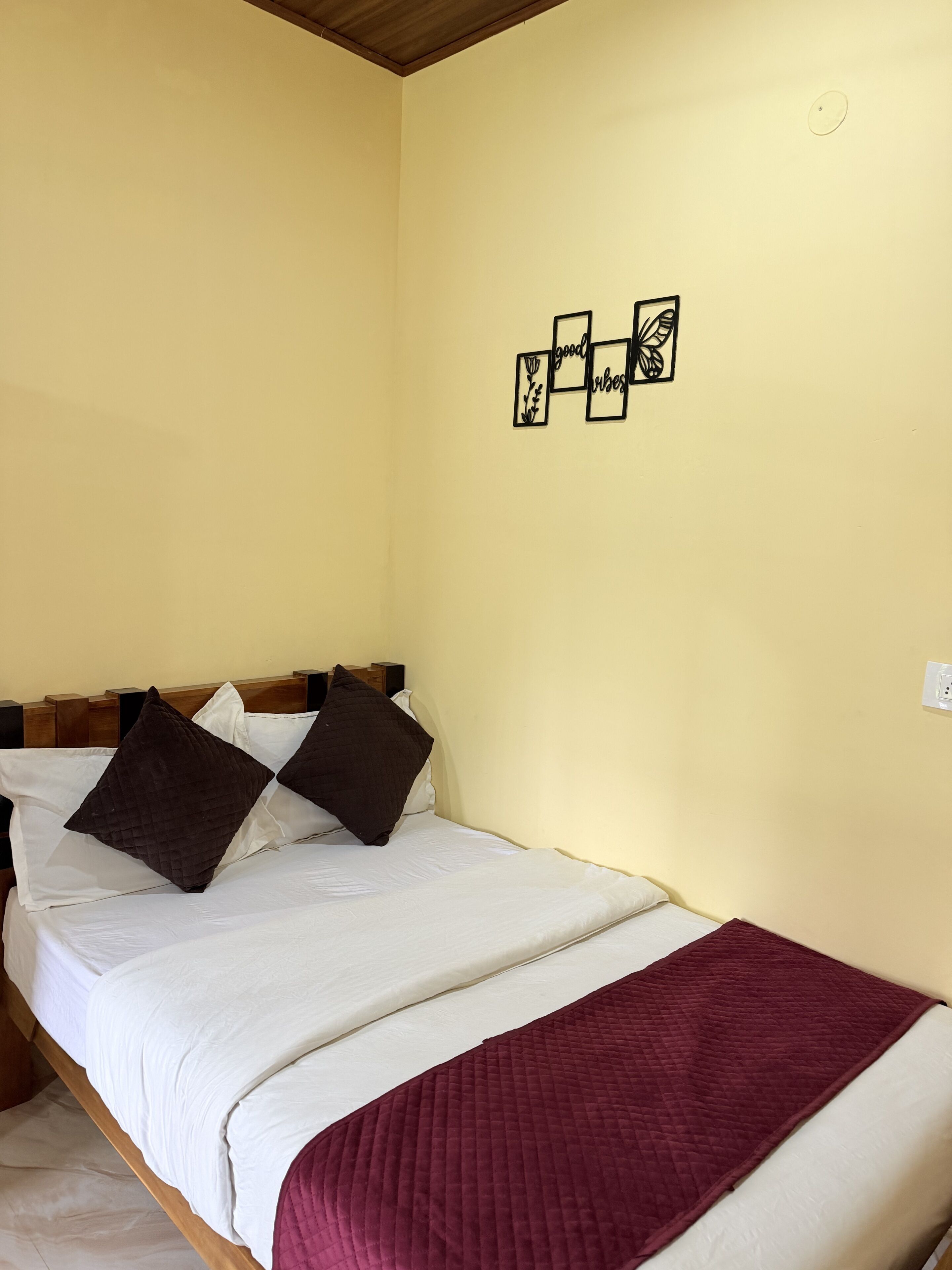 A single bed with a wooden headboard, white bedding, and a maroon quilted throw blanket.