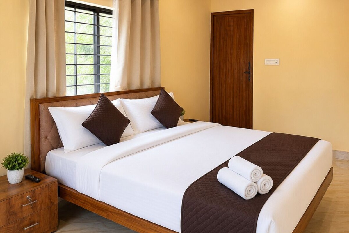 A hotel room with a wooden bed, a ceiling fan, a window with curtains, and a wooden nightstand with a plant.
