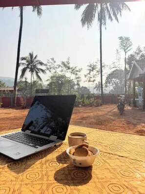 Una computadora portátil sobre una mesa, con un tazón de galletas y una taza, frente a un fondo de palmeras y un sendero de tierra.