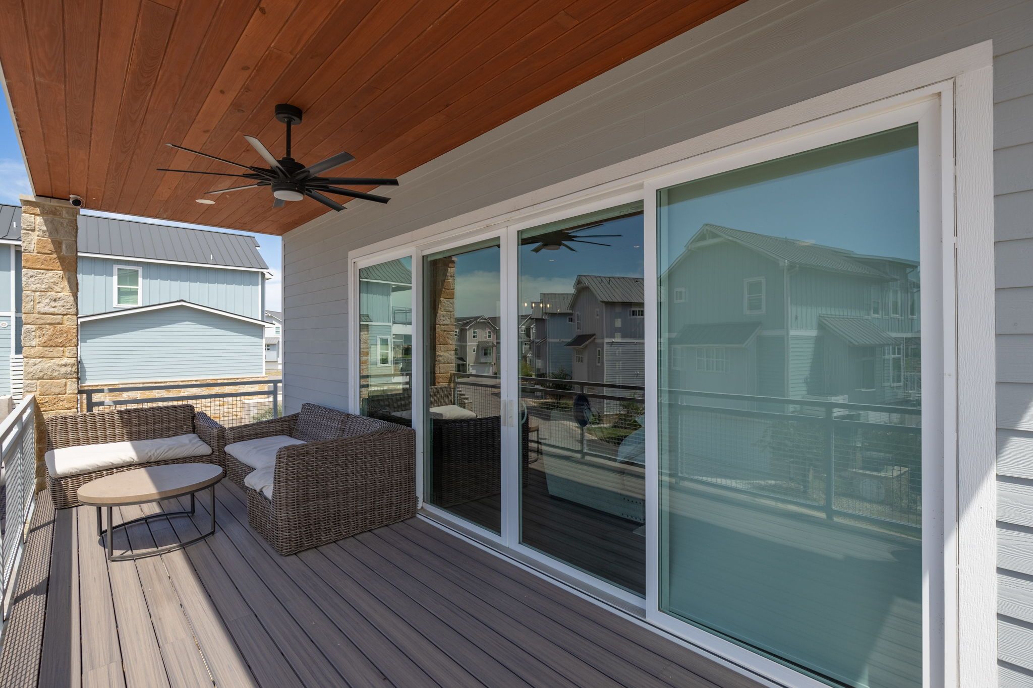 Eine überdachte Terrasse im Freien mit Deckenventilator, Korbmöbeln und einer Schiebetür, die einen Blick auf umliegende Häuser bietet.