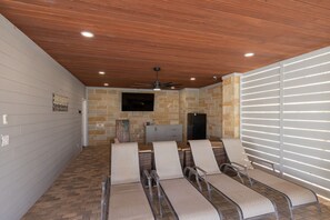A room with a stone wall, a ceiling fan, a flat-screen TV, and a seating area with chairs. - 🌊 New - Lakeview at LBJ - Private Pool, Hot Tub, Sleeps 14 ✨ (Kingsland)