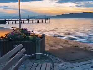 A waterfront view with a wooden bench, a flower planter, and a paved walkway. - Casarão São Chico: A cozy, historic colonial mansion overlooking Babitonga Bay. (São Francisco do Sul)