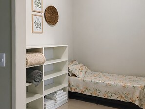 Ein kleines, ordentlich eingerichtetes Schlafzimmer mit einem Einzelbett, einem Einbauschrank mit Regalen und einem Wanddekor.
