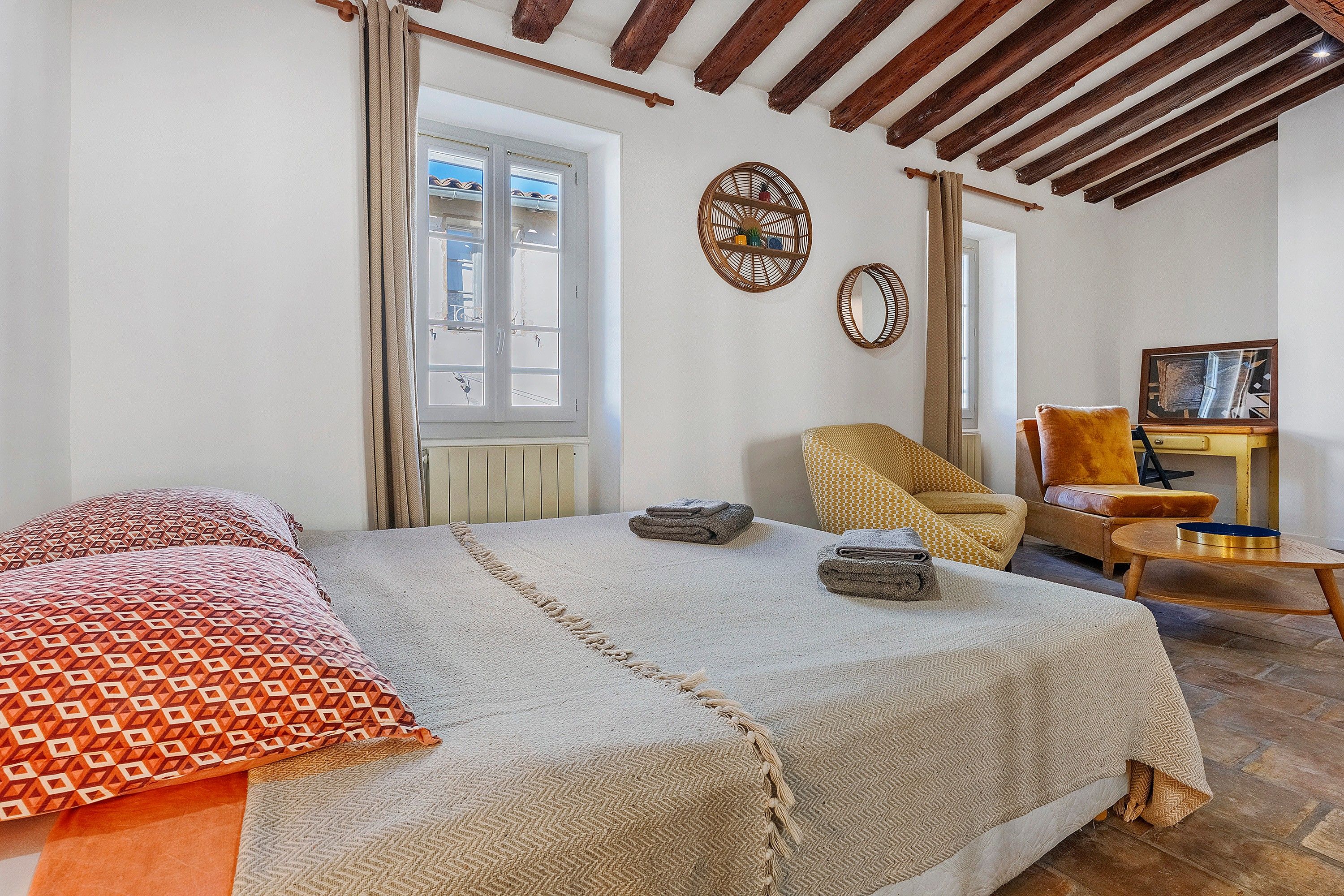 A bedroom with a large bed, a chair, a small table, and a window.