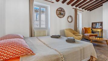 A bedroom with a large bed, a chair, a small table, and a window.