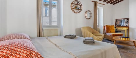 A bedroom with a large bed, a chair, a small table, and a window.