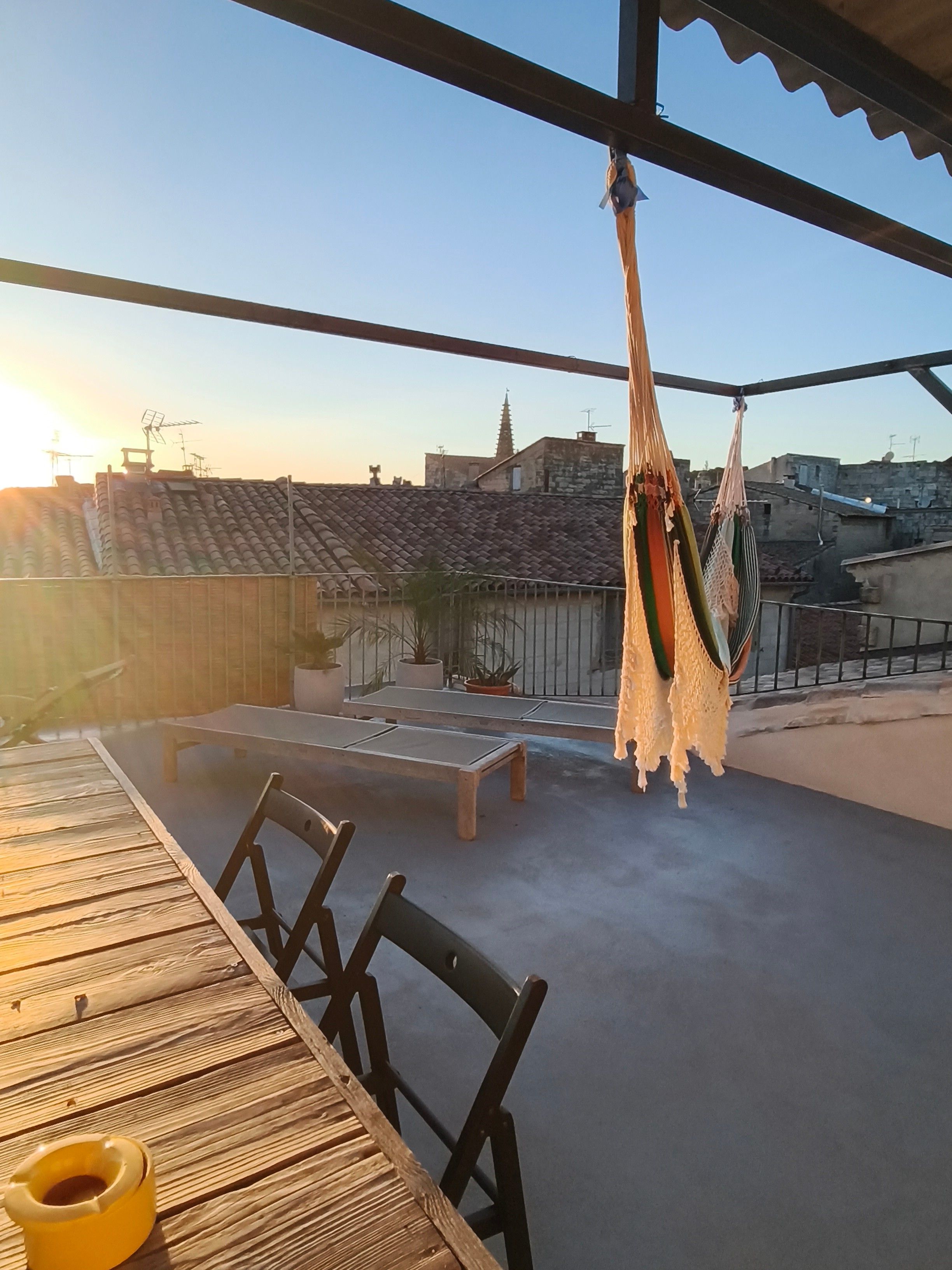 A rooftop terrace with a table and chairs, a hammock, and potted plants.
