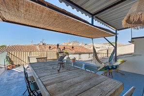 Una terraza en la azotea con una mesa de madera, sillas y una hamaca.