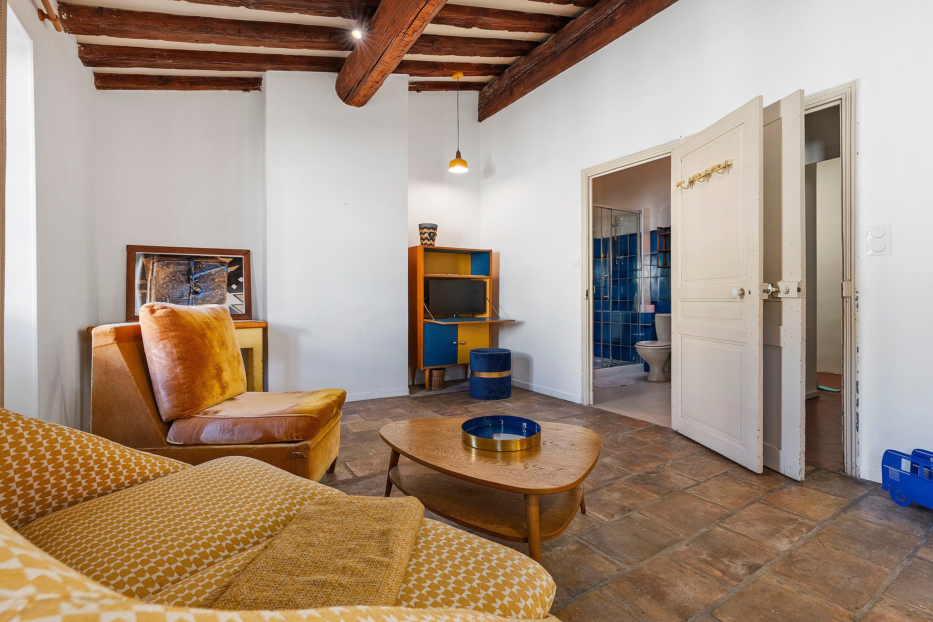 A living room with a sofa, a coffee table, a television, and a door leading to a bathroom.