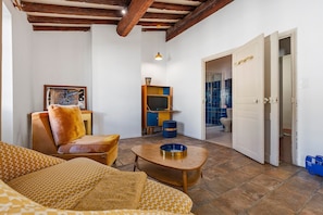Una sala de estar con sofá, una mesa de centro, televisor y una puerta que da a un baño.