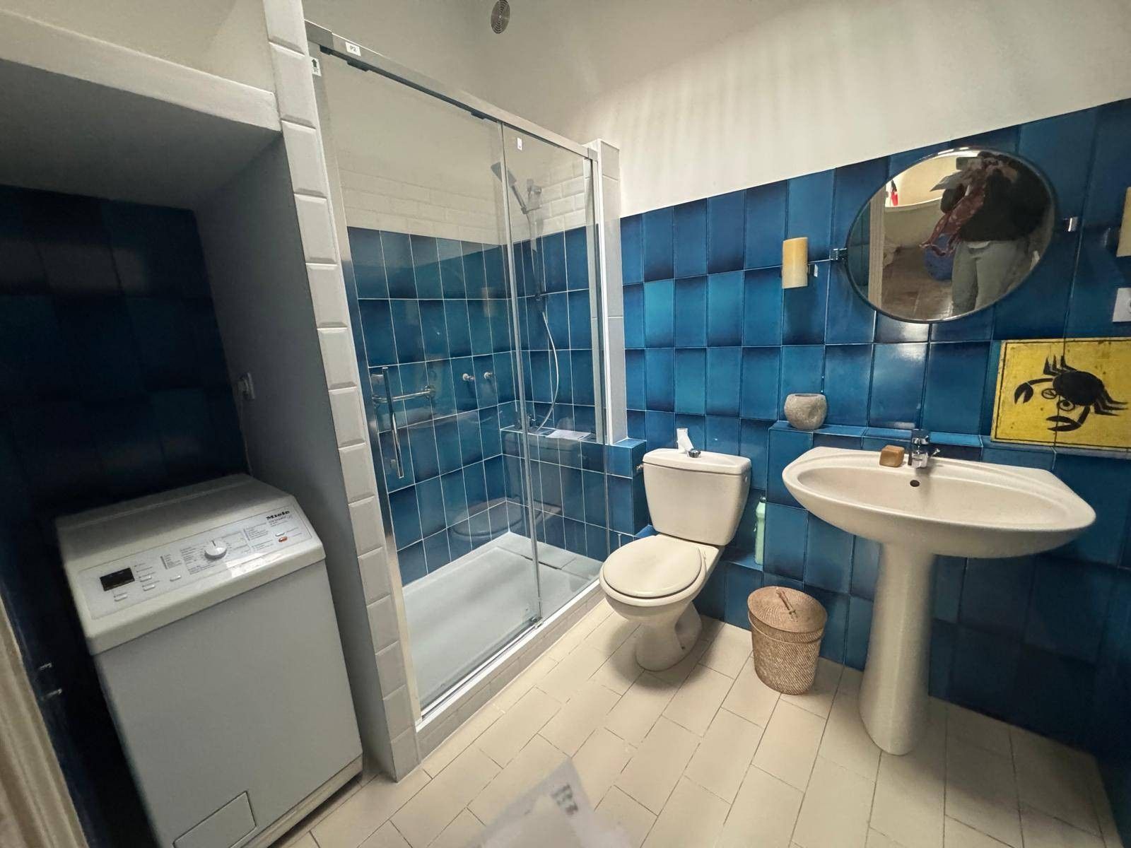 Een badkamer met een glazen douchecabine, toilet, wastafel en een wasmachine.