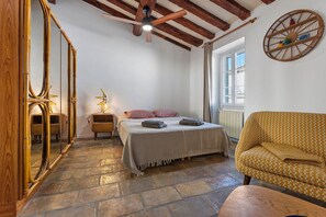 Un dormitorio con una cama, una silla, un espejo y una ventana.