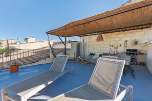 Een dakterras met twee lounge fauteuils, een klein tafeltje, een hanglamp en een barbecue.
