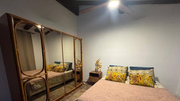 Un dormitorio con cama, un espejo grande, una mesita de noche y un ventilador de techo.