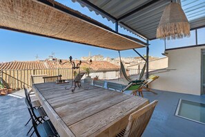 Una terraza en la azotea con una mesa de madera, sillas y una hamaca.