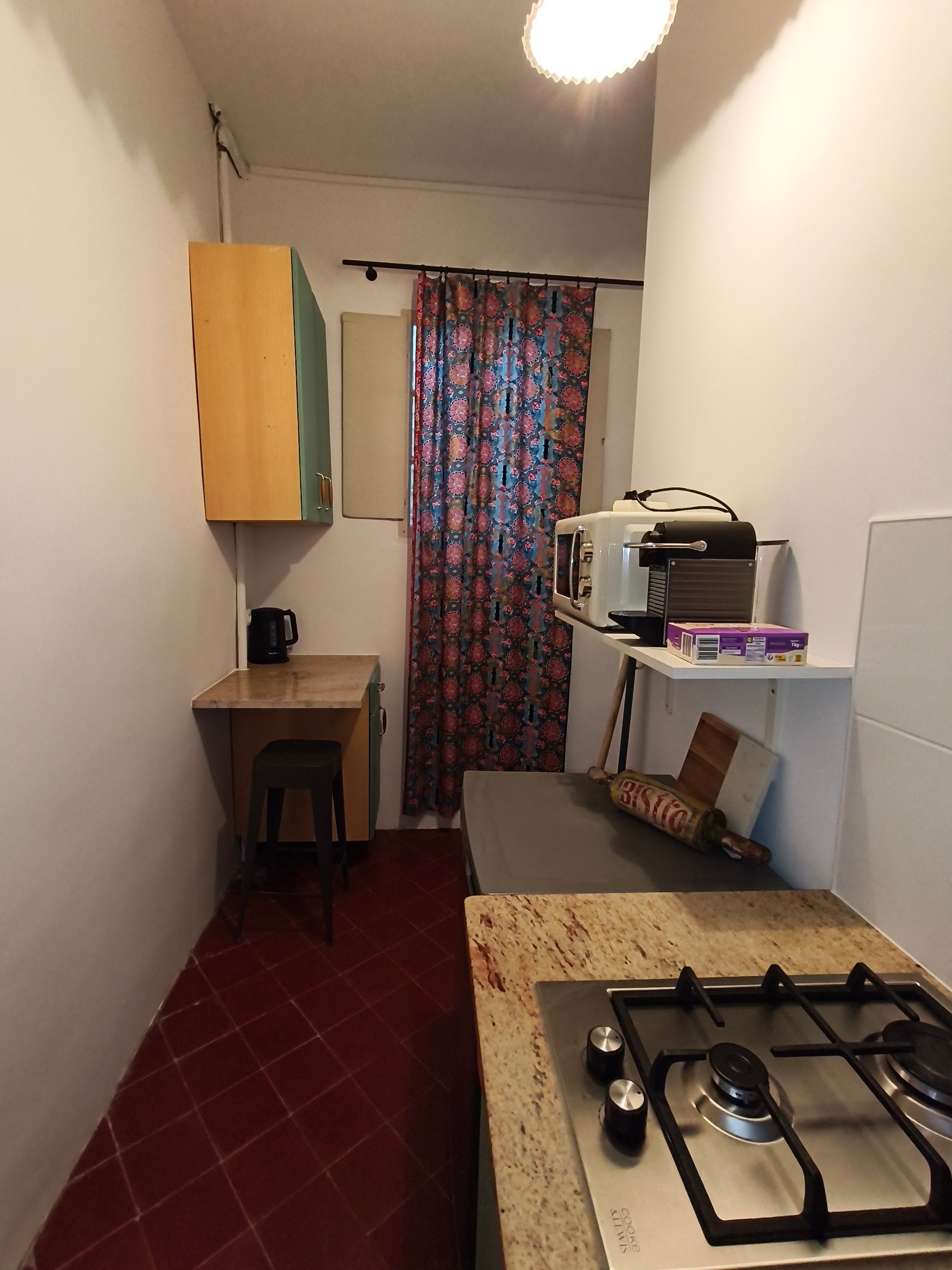 Een kleine keuken met een gasfornuis, een magnetron, een tafeltje en een stoel.