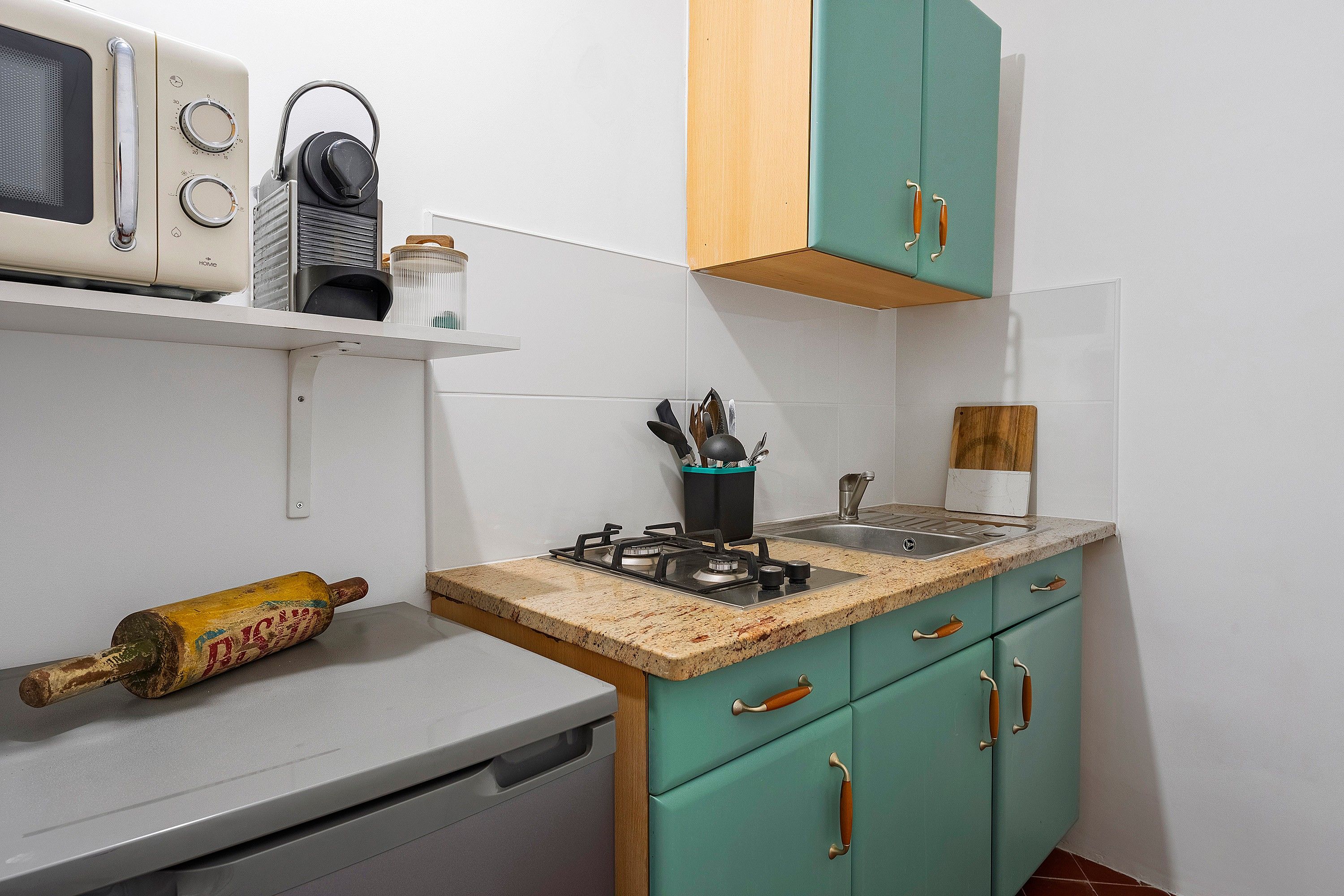 A compact kitchen with a gas stove, a microwave, and a rolling pin on the counter.