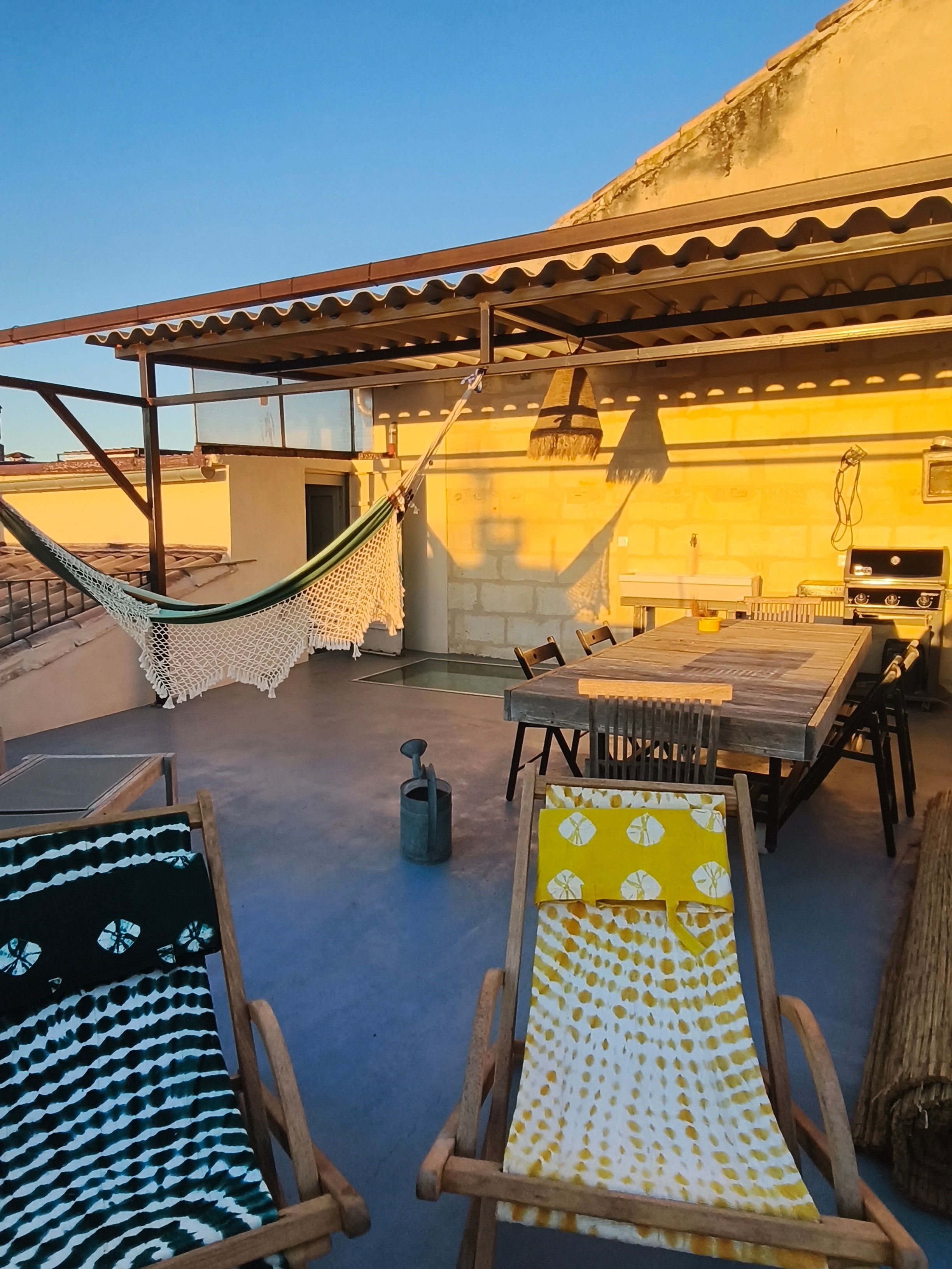 An outdoor patio with a hammock, wooden chairs, a dining table, and a grill.