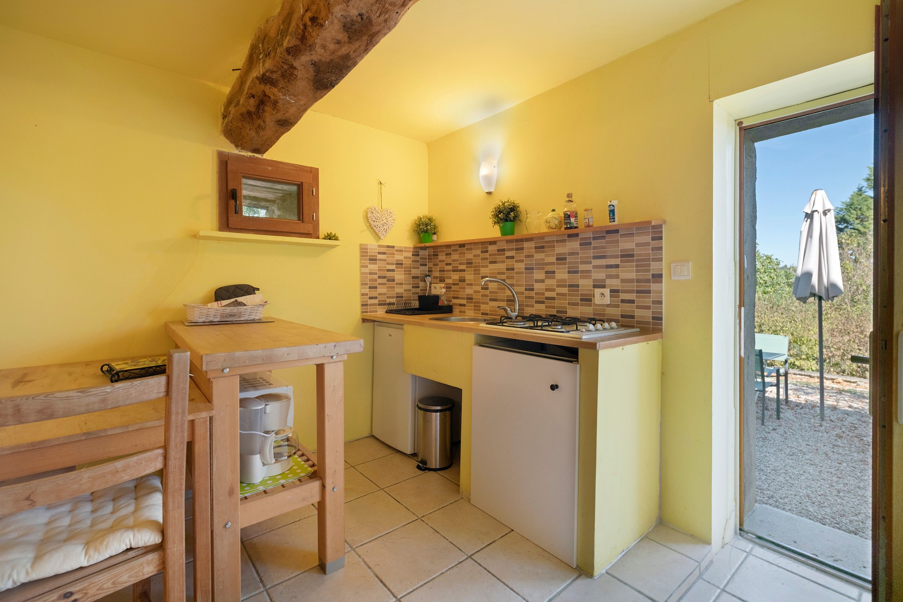 A compact kitchen with a wooden table, a small refrigerator, and a tiled backsplash.