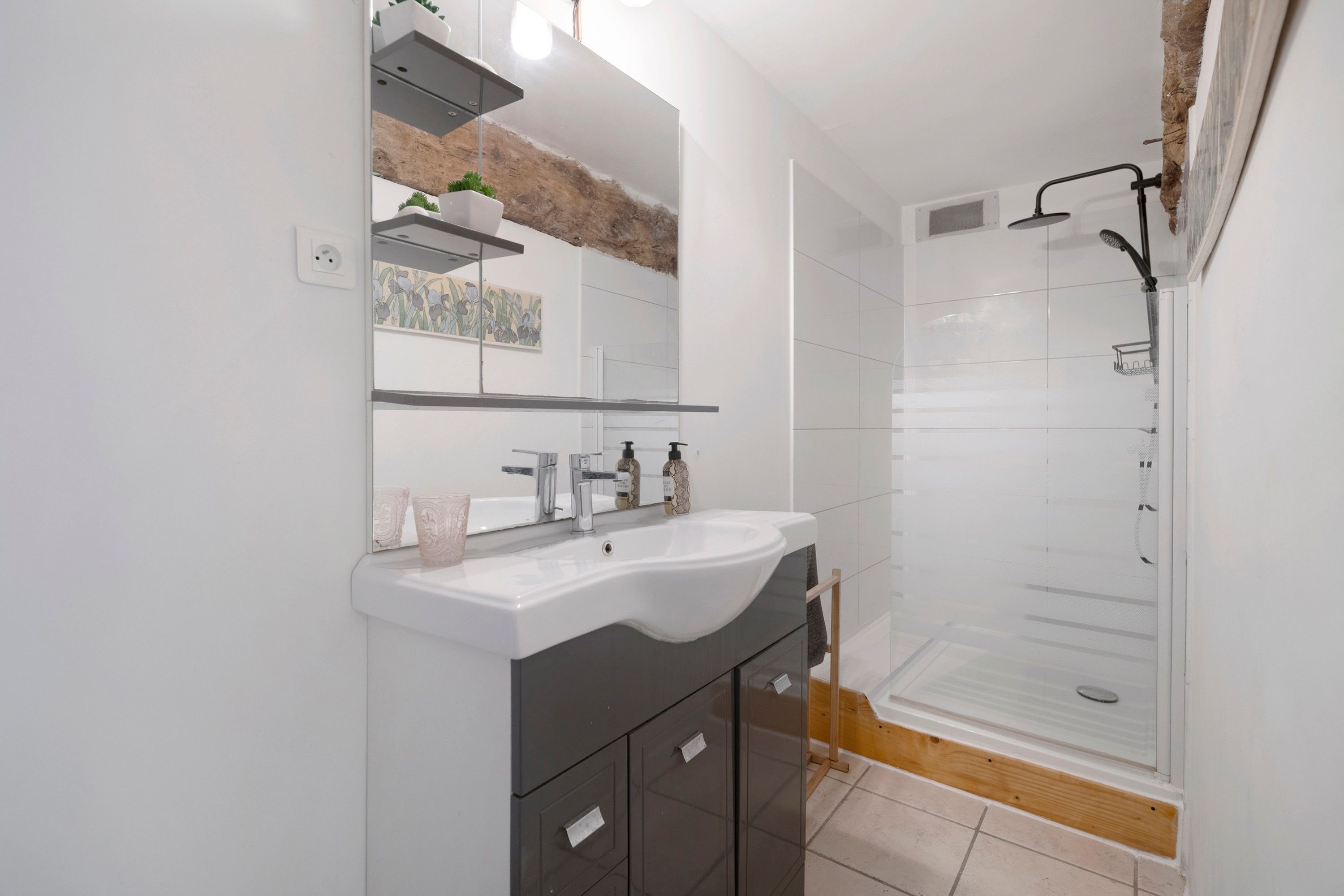 Ein modernes Badezimmer mit einem weißen Waschbecken, dunklen Schränken, einem großen Spiegel und einer Duschkabine aus Glas.