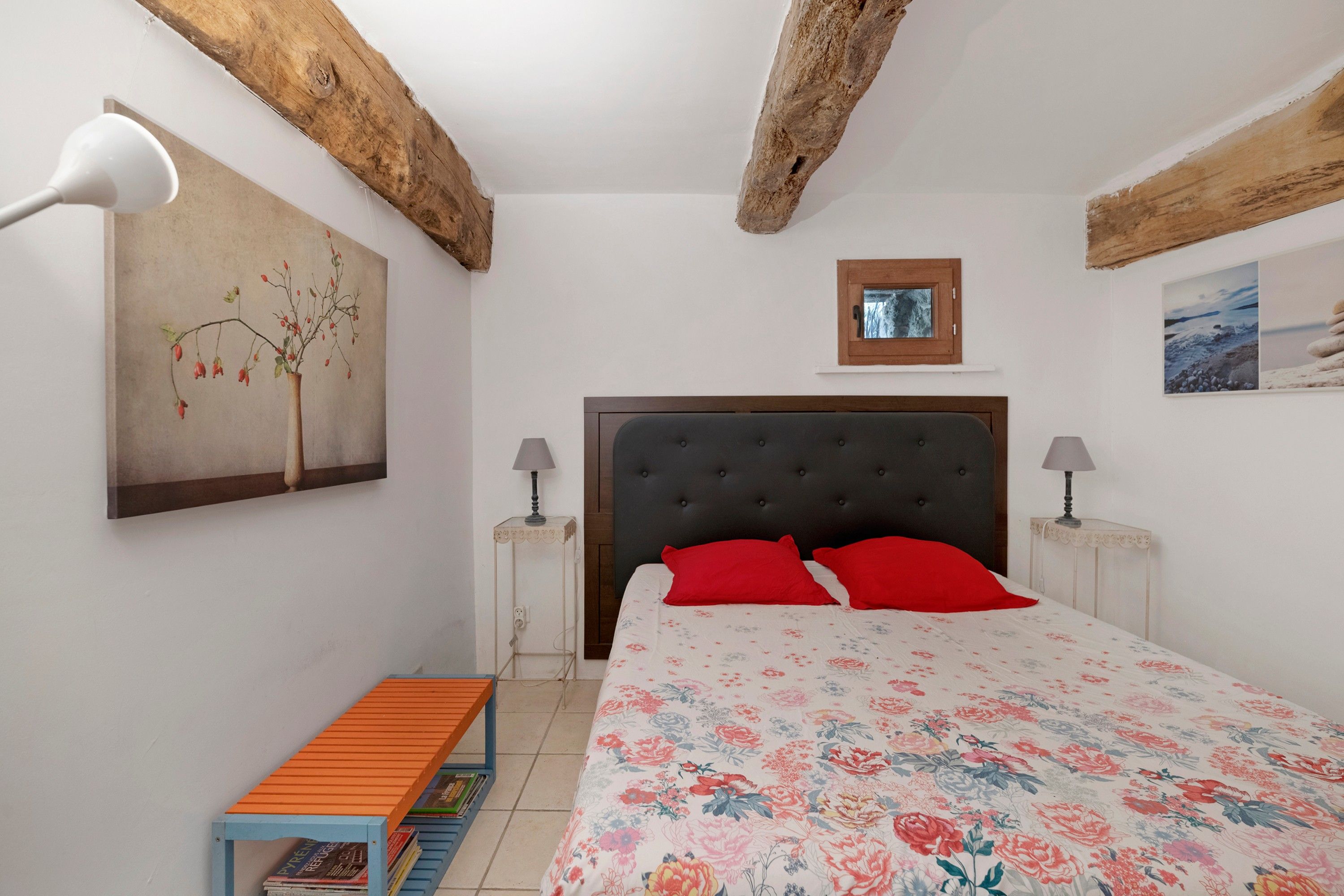 Een slaapkamer met een bed, twee nachtkastjes, een bankje, een schilderij en een raam.